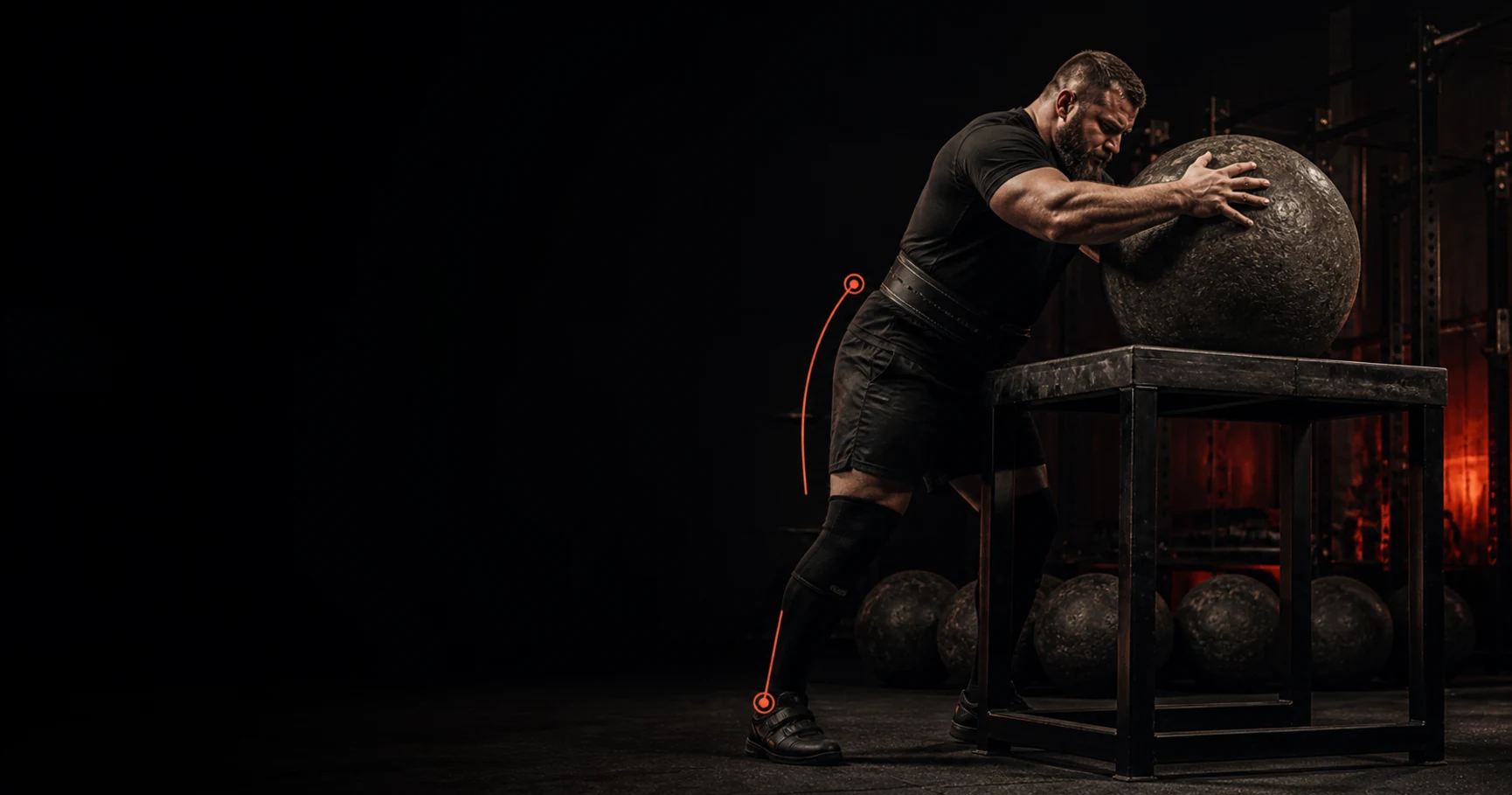 Strongman carries farmer handles through a dark gym with restrained orange accents